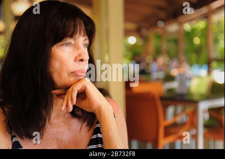 Nahaufnahme der weiblichen Touristenhand, unter ihrem Kinn, mit Blick in die Ferne in einem Restaurant auf Fitzroy Island, Queensland. Stockfoto