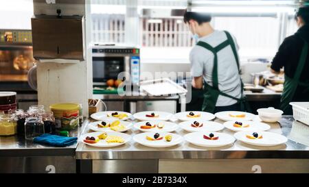 Der Küchenchef bereitet das Frühstücksmenü vor: Omelette, Croissant Sandwich, Banane, apfel und Trauben in weißem Teller auf Holztisch an der Küchenecke. Stockfoto