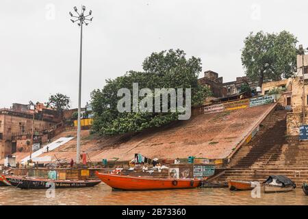 Schwimmende Boote und die Vielfalt der am Ghat lebenden Indianerleute mit alten Gebäuden im Hintergrund entlang des Ganges (Ganga) Flusses in Varanasi. Stockfoto