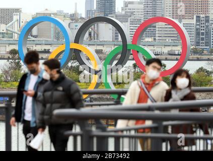 Tokio, Japan. März 2020. Besucher, die Gesichtsmasken tragen, gehen am Freitag, 13. März 2020 vor einem großen Denkmal der olympischen Ringe in Tokio. US-Präsident Donald Trump schlug vor, die Olympischen Spiele in Tokio 2020 im Zuge des Ausbruchs des COVID-19-Coronavirus am 12. März um ein Jahr zu verschieben. Credit: Yoshio Tsunoda/AFLO/Alamy Live News Stockfoto