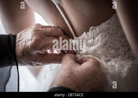 Detail der Hände einer älteren Mutter, die das Hochzeitskleid knöpfen. Morgendliche Vorbereitungen. Frau, die sich kleidet. Stockfoto