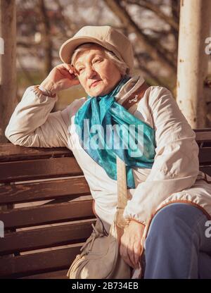 Eine elegante ältere grauhaarige Frau sitzt auf einer Parkbank. Stockfoto