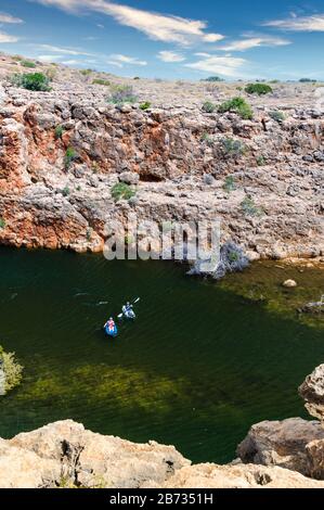 Blick von der Felswand hinunter auf die Yardie Creek Gorge und die Felswand von Western Australia, mit zwei Abenteuerskipaddlern, die den Bach durchfahren. Stockfoto