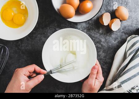 Weiße Eier mit Schneebesen in einer Palte schlagen. Draufsicht über die Hände der Frau, die Eier mischt. Stockfoto