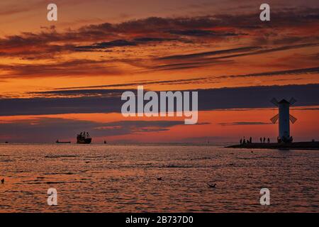 Sonnenuntergang mit Silhouetten von Touristen auf dem Windmühlenförmigen Leuchtturm an der Ostsee in Swinemünde. Swinoujscie, Polen Stockfoto