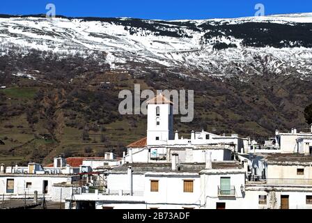 Blick über die Dächer der Stadt in Richtung unserer Lieben Frau der Hauptkirche und schneebedeckte Berge der Sierra Nevada, Capileira, Spanien. Stockfoto