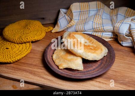 Tonplatte mit zwei einzelnen gebratenen Pasteten mit Fleisch auf Holztisch. Tatarische traditionelle Pasteten. Stockfoto