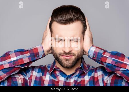 Frustrierter, gutaussehender Mann, der seine Ohren bedeckt und die Hände vor grauem Hintergrund stehen. Stockfoto