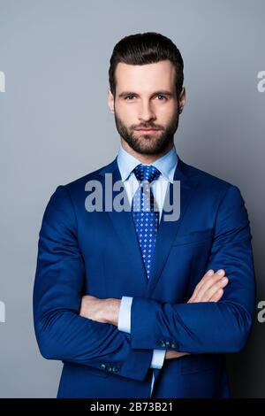 Portrait eines ernsthaften, trendigen Mannes in blauem Anzug und Krawatte, die die Hände kreuzen und die Kamera betrachten. Stockfoto