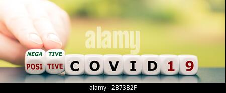 Testergebnis eines Corona-Tests. Hand dreht einen Würfel und ändert den Ausdruck "positive COVID19" in "negative COVID19". Stockfoto