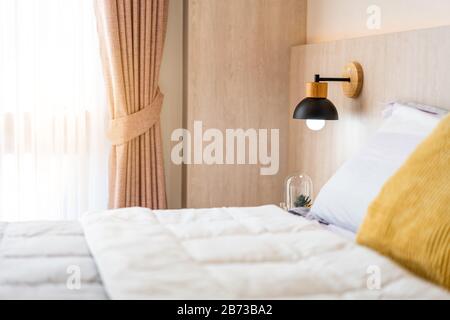 Stilvolle Nachttischlampe aus Holz, schwarz, Holzbett und graue Decke im Schlafzimmer. Komfortables und elegantes Innendesign für eine gemütliche Atmosphäre. Stockfoto