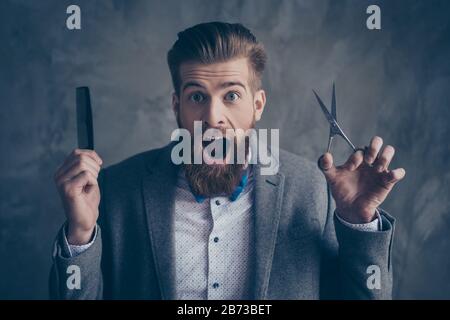 Selbstbewusster, stilvoller überraschter Mann im Anzug und mit dem Bogen, der zwischen Schere und Kamm wählt. Brutaler, aufgeregter Flusspferd mit schwerem, dickem Bart, bereit zum barbier Stockfoto