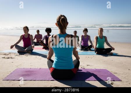 Rückansicht des Yoga-Lehrers, der am Strand eine Yoga-Sitzung macht Stockfoto