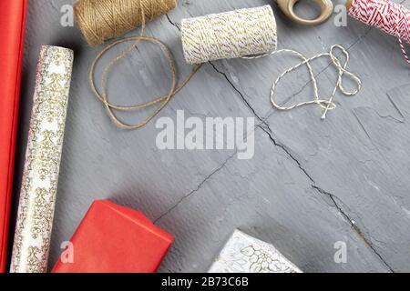Vorbereitung auf die Verpackung von Geschenken, auf dem Tisch aufgelegtes rot-weißes Verpackungspapier, Fäden verschiedener Farben für Wicklung und Schere Stockfoto