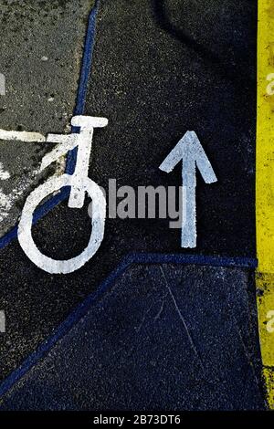 Weiße Fahrtrichtungs- und Radwegschilder mit gelber Kantenlinie gegen den Asphalt Stockfoto