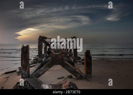 Blick auf zerbrochene alte Struktur Überreste von Pier im Meer. Kleine Welle krachend in die texturierten rostigen Pier Pfosten in der während der schönen Twiligh Stockfoto