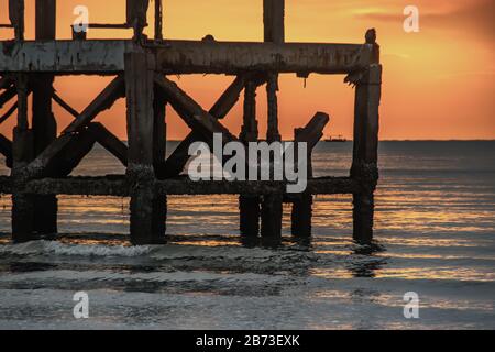 Blick auf zerbrochene alte Struktur Überreste von Pier im Meer. Kleine Welle krachend in die texturierten rostigen Pier Pfosten in der während der schönen Twiligh Stockfoto