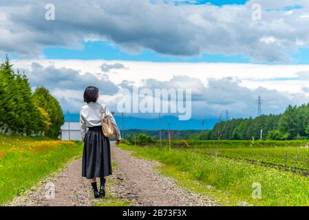 junges asiatisches Mädchen, das an einem sonnigen Tag auf einer Landstraße spazieren geht Stockfoto