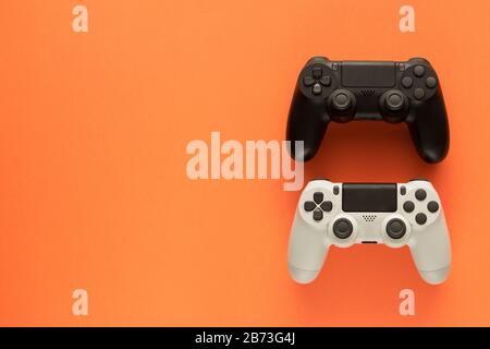 Stock-Foto von zwei Gamepads auf orangefarbenem Hintergrund und Kopierbereich auf der linken Seite Stockfoto