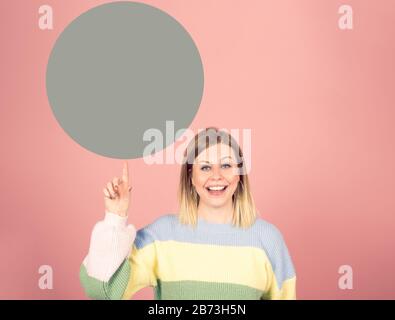 Lächelnde, fröhliche junge Frau, die den Finger nach oben zu einem grünen Kreis zeigt Stockfoto