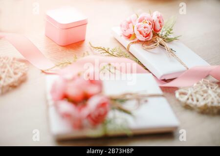 Geschenkboxen mit einfachen weißen Handwerk Papier und Strauß von Rosen und grünen Zweig verpackt. Kleine rosa geschenkbox und rosa Band. Stockfoto