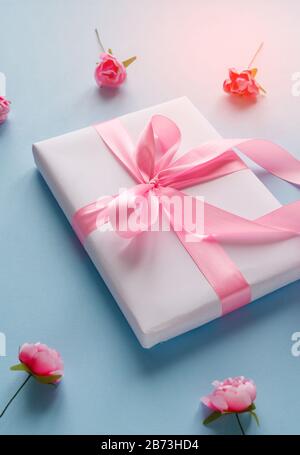 Frühlingsdekor aus kleinen rosa Rosen. Weiße Geschenkbox mit einem rosa Band. Stockfoto