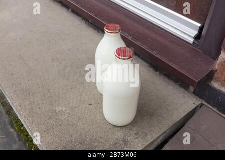 Frische Milch in recyclingfähigen Glasspint Flaschen, die von einem traditionellen Milchmann an die Tür geliefert werden Stockfoto