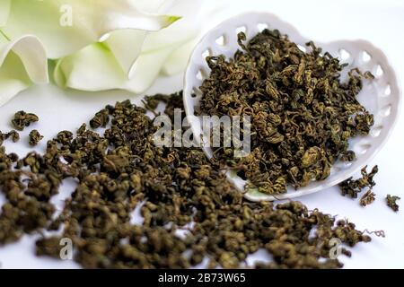 Trockene grüne Teekräuter mit Blumen und Vintage-Porzellan-herzförmige Platte auf weißem Hintergrund. Stockfoto