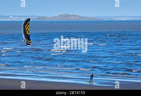 Portobello Beach, Edinburgh, Schottland, Großbritannien. März 2020. Man Skateboard Kitesurfing entlang des ungewöhnlich ruhigen Sandstrands. Sonnig aber kühl, Wind: ENE 18 km/h mit Windböen von 32 km/h, Temperatur von 6 Grad Celsius. Stockfoto