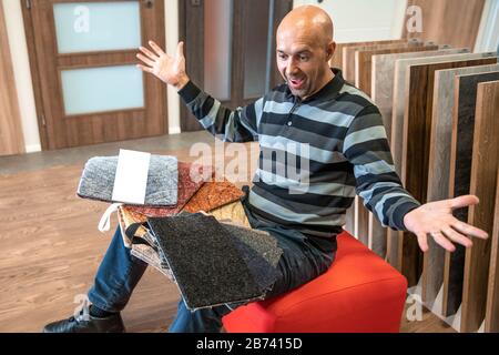 Der Mann wählt die Farbe des neuen Teppichs nach den Proben im Bodenbelaggeschäft Stockfoto