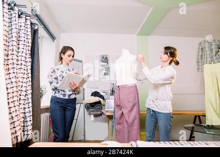 Porträt von zwei jungen Frauen Modedesignern oder Schneidern, Messung von Schaufensterpuppen, Haltestreifen, Arbeit mit Dummy im gemütlichen Kreativ-Studio oder im Schwanz Stockfoto
