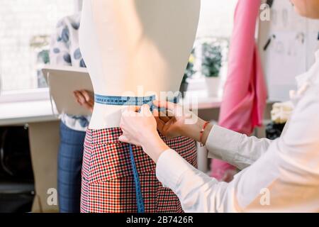 Designstudio. Hosen an Mannequin und Maßband in Frauenhand. Dressmacher, der Dummy, Mannequin Messungen mit Maßband in der Werkstatt vornimmt, Stockfoto