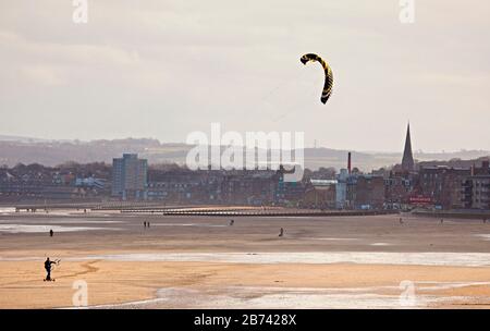 Portobello Beach, Edinburgh, Schottland, Großbritannien. März 2020. Man Skateboard Kitesurfing entlang des ungewöhnlich ruhigen Sandstrands. Sonnig aber kühl, Wind: ENE 18 km/h mit Windböen von 32 km/h, Temperatur von 6 Grad Celsius. Stockfoto