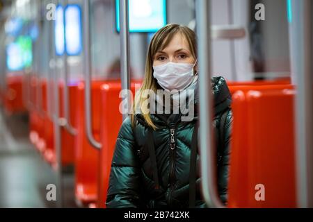Frau im Winter Mantel mit Schutzmaske im Gesicht sitzend im U-Bahn-Auto, telefonieren, besorgt aussehen. Vorbeugende Maßnahmen an öffentlichen Orten Stockfoto