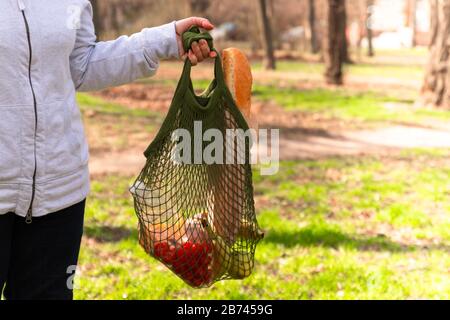 Weibliche Hand halten Sie eine grüne Eco-Baumwolle Saite mit Bio-Lebensmitteln. Gesungene Tomaten, Bananen, Äpfel, Brot und Käse auf verschwommenem Hintergrund. Kein Abfall Stockfoto