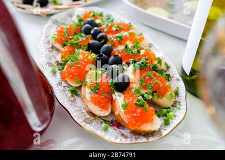 Vorspeise mit Brot, Butter und rotem Kaviar. Sandwiches mit Kaviar, dekoriert mit Oliven und grünen Zwiebeln. Ein Gericht auf dem Tisch zum Feiern. Stockfoto