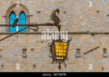 Eine kunstvolle Glasstraßenlampe, die von einem mythischen Wesen aus Metall in der historischen Altstadt von Volterra, Toskana, Italien, gehalten wird. Stockfoto