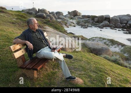 Ein älterer Mann sitzt auf einer Bank am Meer Stockfoto
