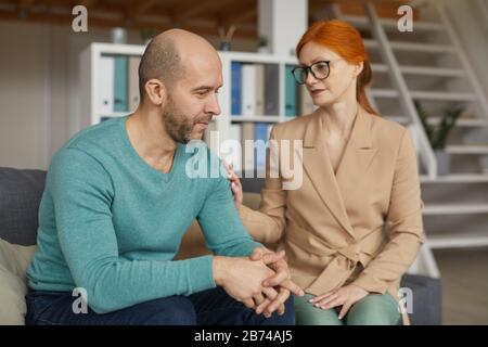 Trauriger reifer Mann, der zusammen mit der Frau auf dem Sofa sitzt und ihn bei seinem Besuch unterstützt Stockfoto