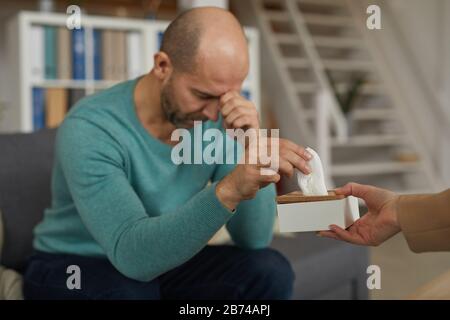 Ärgerlicher Mann, der auf dem Sofa sitzt und die Serviette nimmt, was die Frau vorschlägt Stockfoto