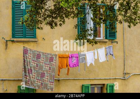 Farbenfrohe Nasswäsche, die im Mai auf einem zwischen zwei Fenstern gelegenen Hügel in der Stadt Volterra, Provinz Pisa, Toskana, Italien, trocknet. Stockfoto