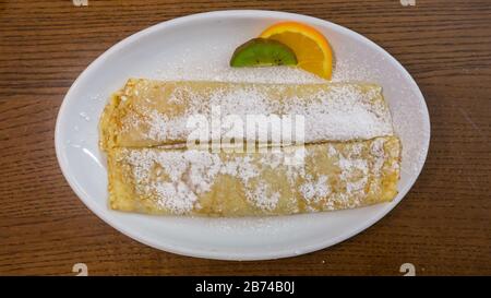 Blick auf zwei frisch zubereitete Palatschinken. Eingewickelt und mit gepudertem Zucker bestreut. Ungarische Spezialität, ähnlich wie Crepes. Gefüllt mit Marmelade. Stockfoto