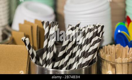 Panorama mit schwarz-weiß gestreiften Trinkhalmen in einer metallischen Schüssel. Auf den rechten Holzstöcken, in den hinteren Kaffeetassendeckeln. Kaffeeausrüstung. Stockfoto