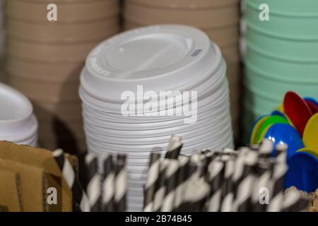 Deckel/Deckel für weiße Kaffeetasse. Aus Kunststoff, übereinander gestapelt. Strohhalme im Vordergrund, Becher im Hintergrund. Stockfoto