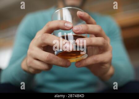 Nahaufnahme des Mannes, der Glas mit Alkohol in den Händen hält, er sitzt und entspannt sich nach der Arbeit Stockfoto