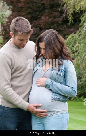 Schwangere junge Frau, die mit ihrem Partner steht und ihren Bauch zersäumt Stockfoto