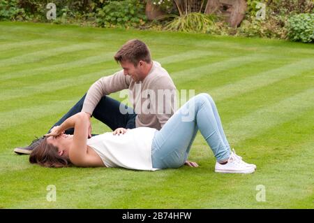 Schöne schwangere junge Frau, die sich auf dem Gras aufliegt und ihre Partnerin neben ihr sitzt Stockfoto