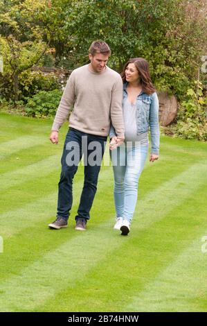 Schwangere junge Frau, die mit ihrem Partner die Hände hält Stockfoto