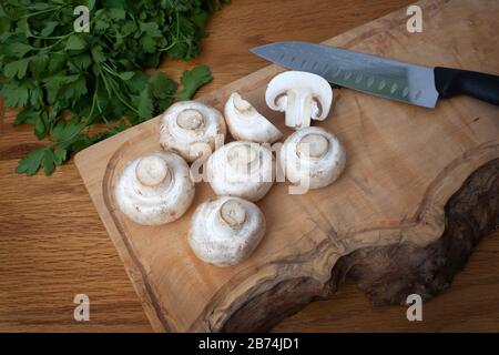 Gemeine weiße Pilze auf einem Hackbrett mit flacher beblätterter Petersilie Stockfoto