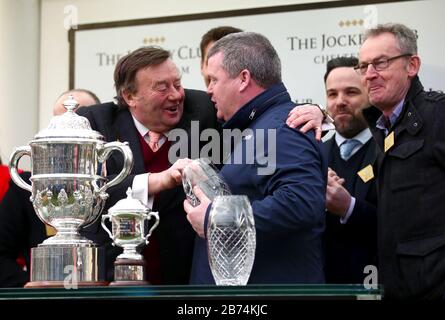 Trainer Gordon Elliott (zweite rechts) wird von Nicky Henderson mit der Trophäe überreicht, nachdem er den Johnny Henderson Grand Annual Challenge Cup Handicap Chase mit Chosen Mate während des vierten Tages des Cheltenham Festivals auf der Cheltenham Racecourse gewonnen hat. Stockfoto